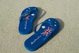 A pair of blue Australia day thongs with national flag design on a sandy beach.
