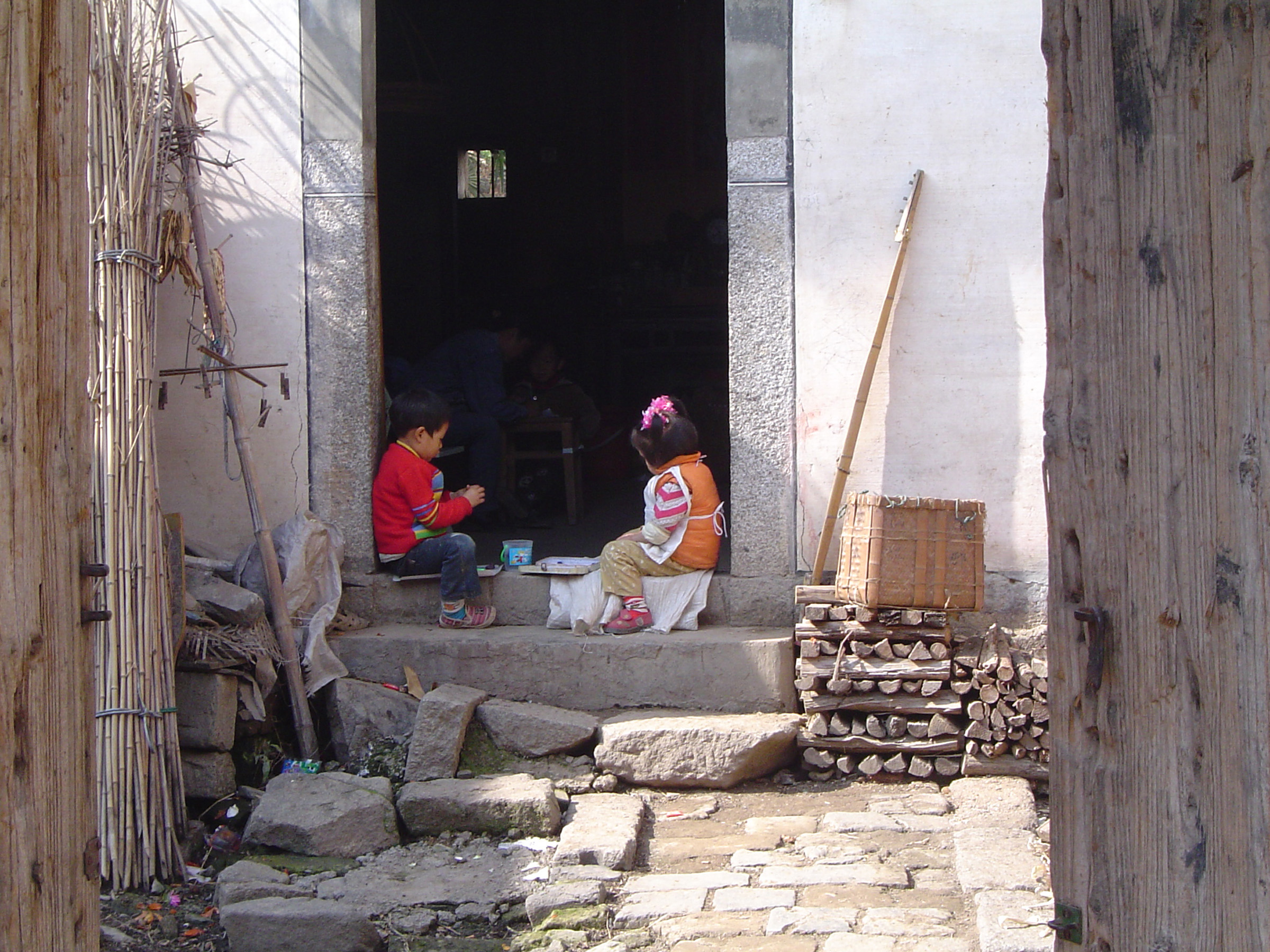 an image of Two Kids Playing at the Door Step of Vintage Ordinary Chinese House in China.