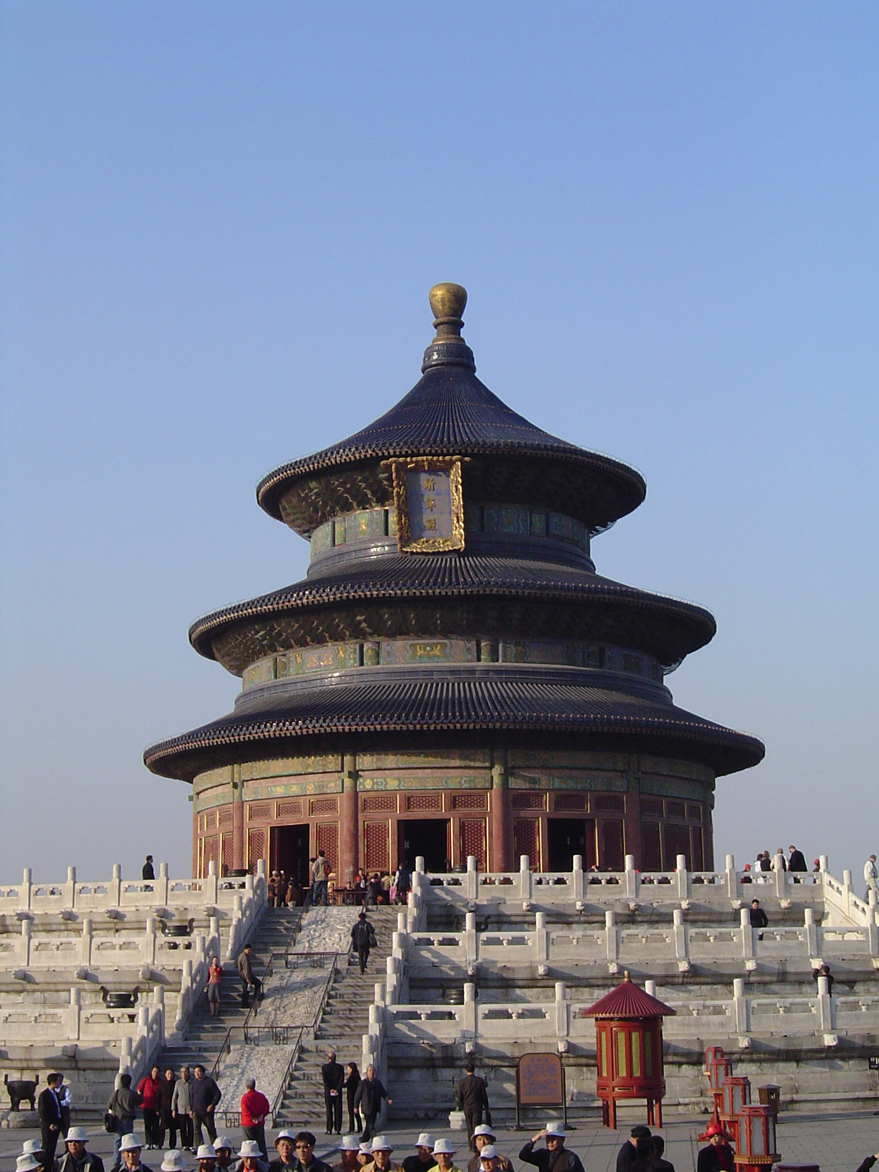 an image of Famous Huge Historic Temple of Heaven in China, Known as Hall of Prayer for Good Harvests. Captured with Random Visitors on Light Blue Gray Sky Background.