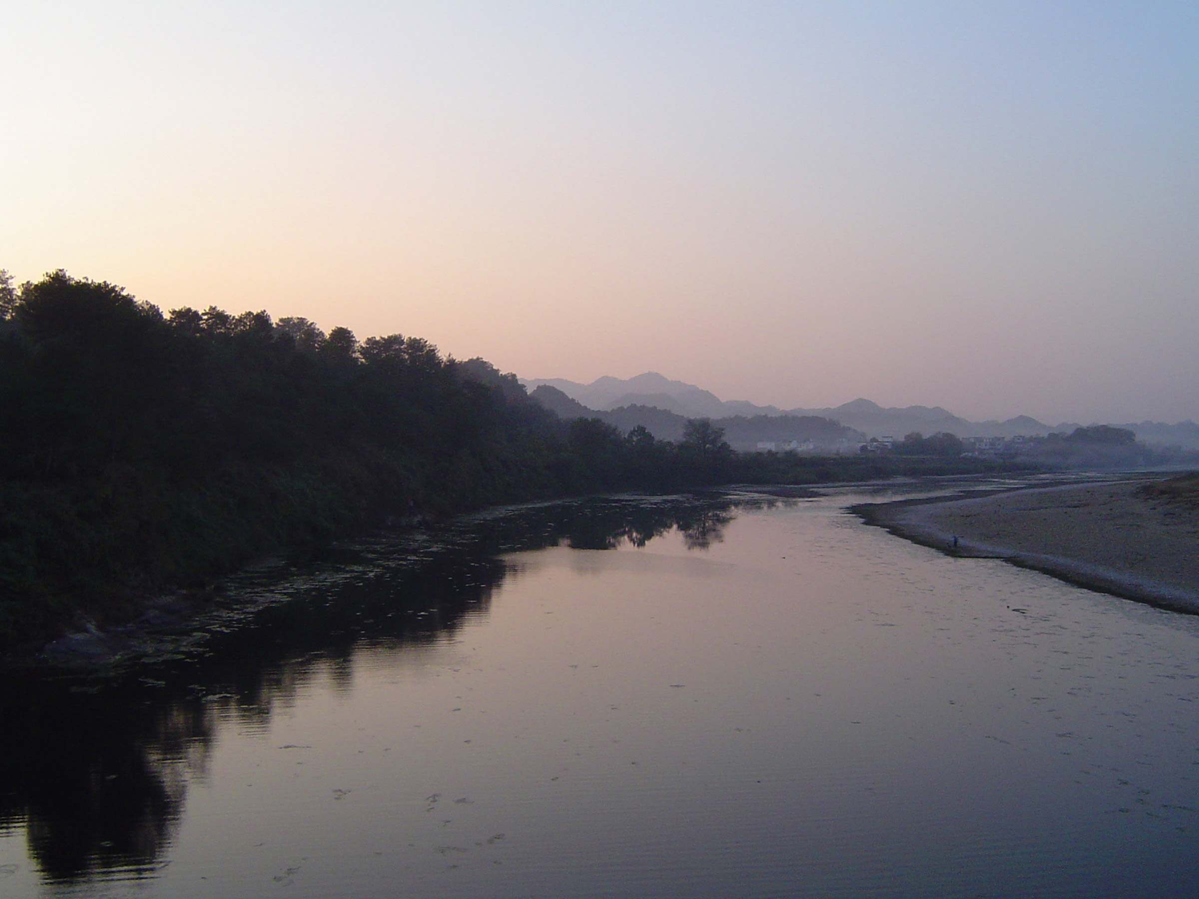 an image of Tranquil misty estuary at dusk with the forest and distant mountains mirrored in the calm water
