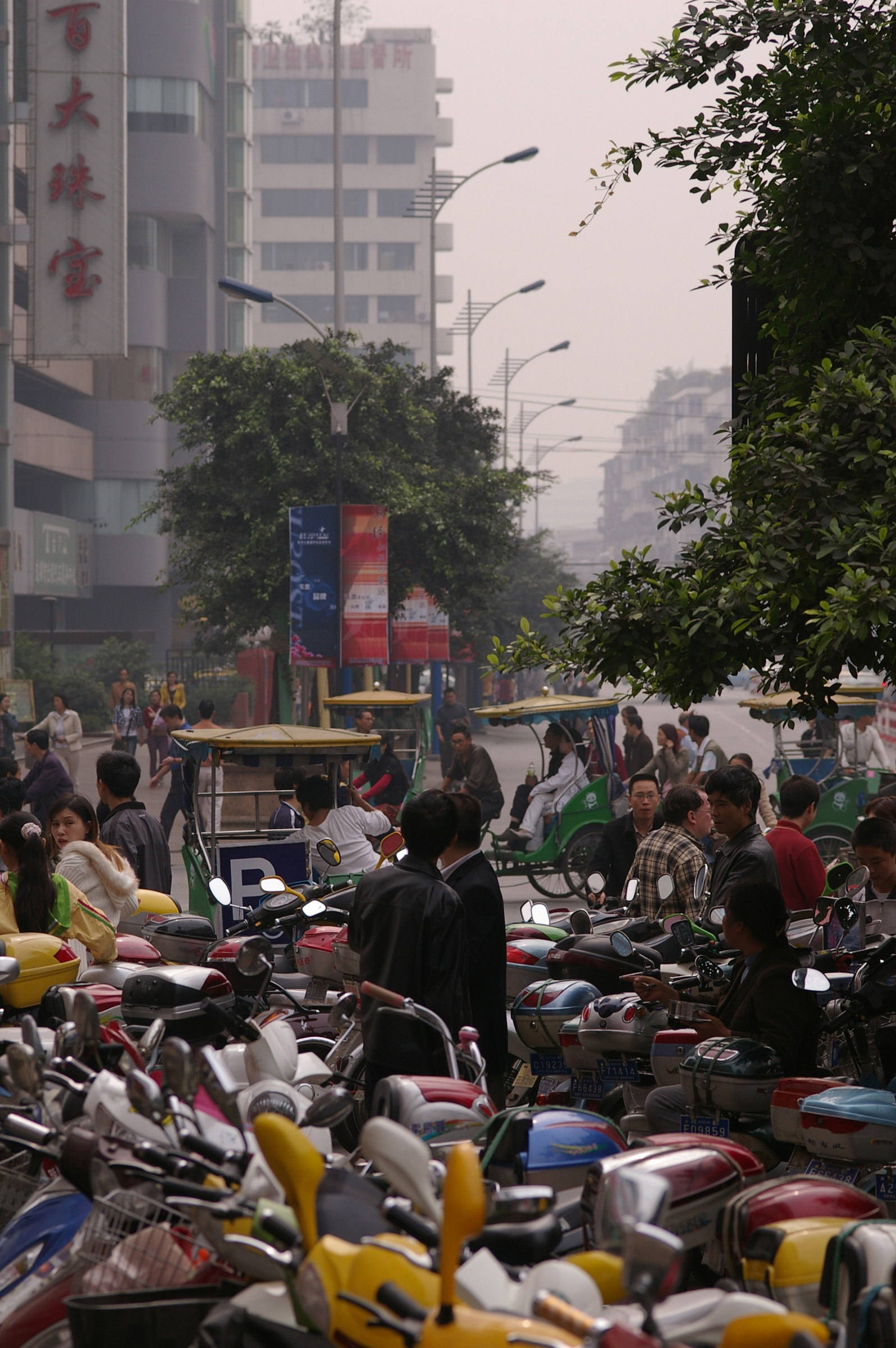 an image of Plenty of Assorted Motorcycles Parked at the City Parking Area Captured with Random Chinese People.