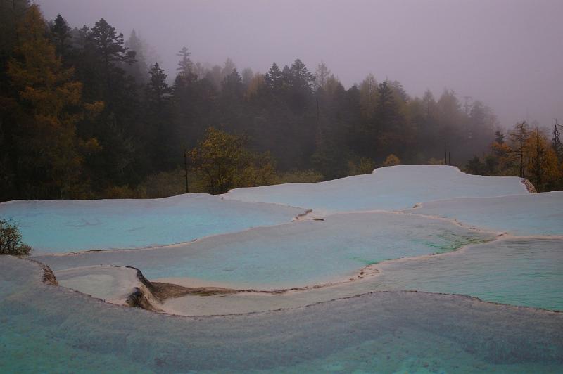Hot therapeutic thermal pools in China encrusted with natural mineral deposits from the water surrounded by misty evergreen forests in a scenic landscape