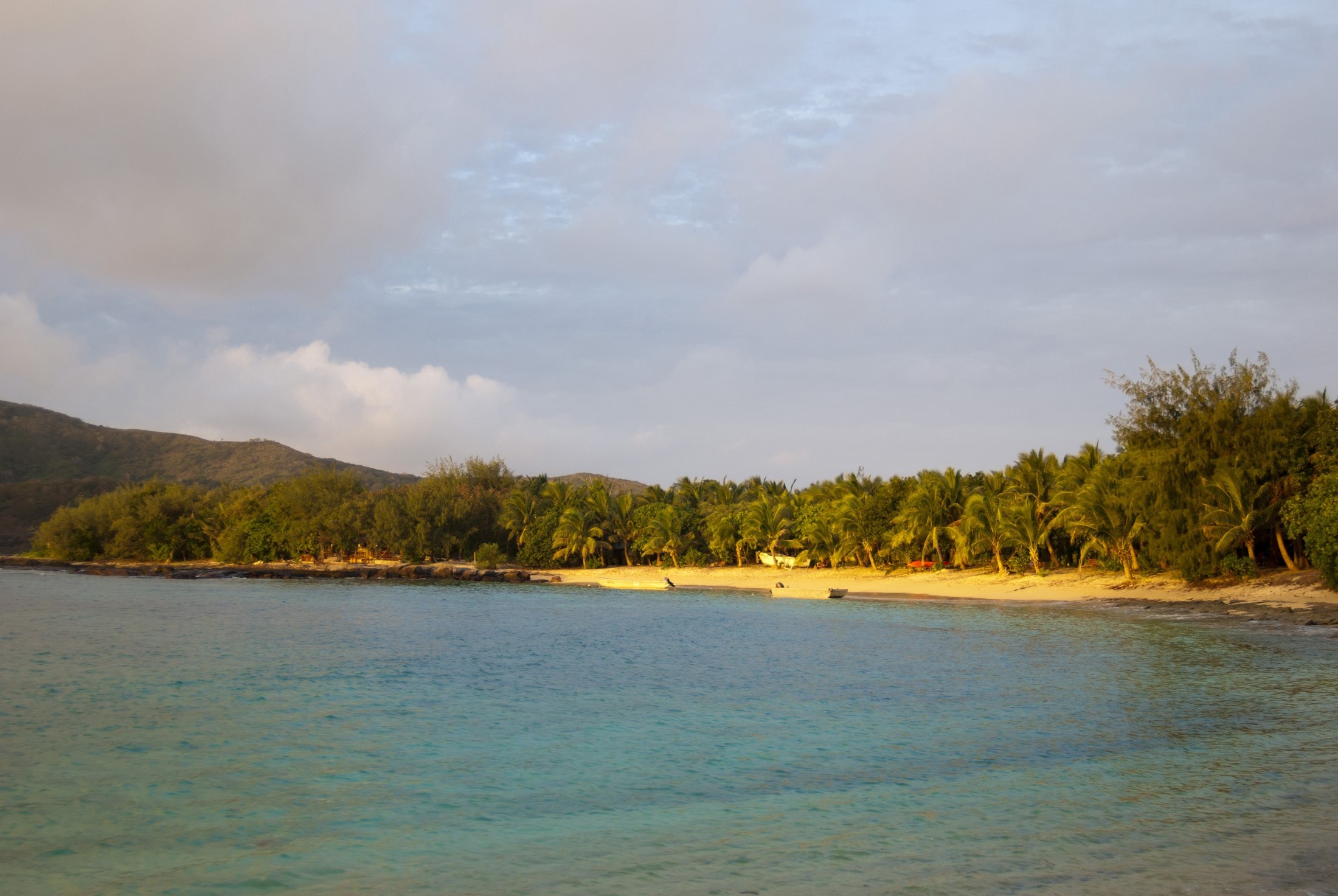 an image of View over a calm sea to a sunset on a tropical beach with the golden glow lighting the sand and lush green vegetation