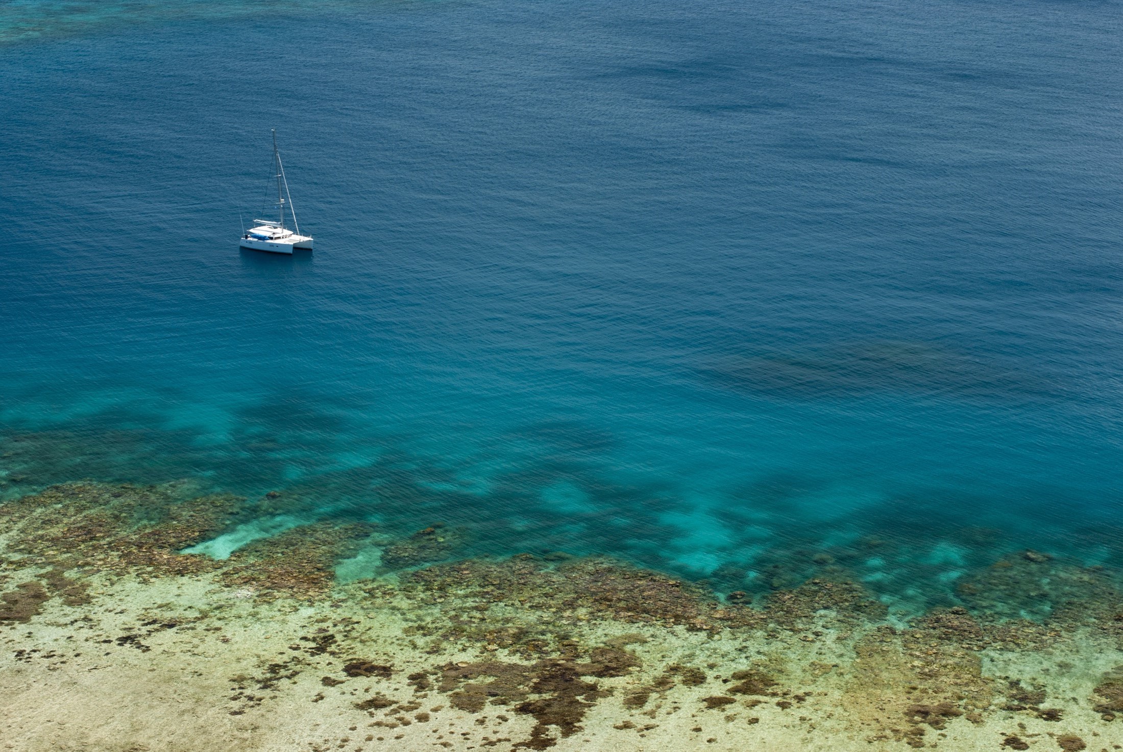 an image of Blue ocean and crystal clear shallows off Yasawas Island, Fiji with a yacht passing close to shore and copyspace