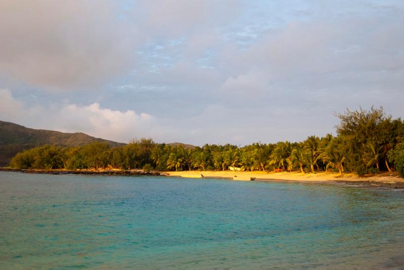 View over a calm sea to a sunset on a tropical beach with the golden glow lighting the sand and lush green vegetation