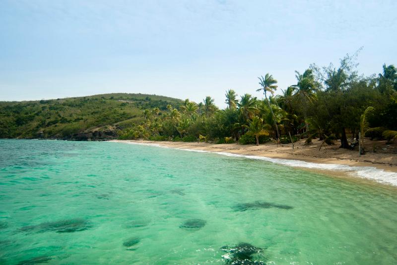 Beautiful clear water in a tropical bay and coastline with sandy beach and backdrop of palm trees