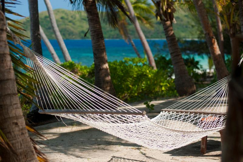 Empty hammock strung from palm trees overlooking a blue ocean on an idyllic tropical island