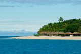 Thatched traditional beach umbrellas on Bounty island, Fiji, on a sunny sandy tropical beach with palm trees
