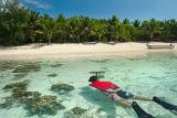 Man snorkeling off a tropical island floating over a shallow reef in crystal clear water