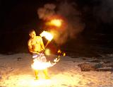 Shirtless barefoot fire dancer on Fiji twirling flaming sticks during a night performance on a sandy beach