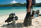 Cropped view image of a man going scuba diving holding a pair of flippers with air tanks and equipment propped up on the beach alongside him