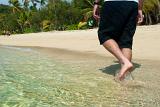 Cropped view of the legs of a man walking through clear sparkling shallow surf on a sandy tropical beach in sunshine