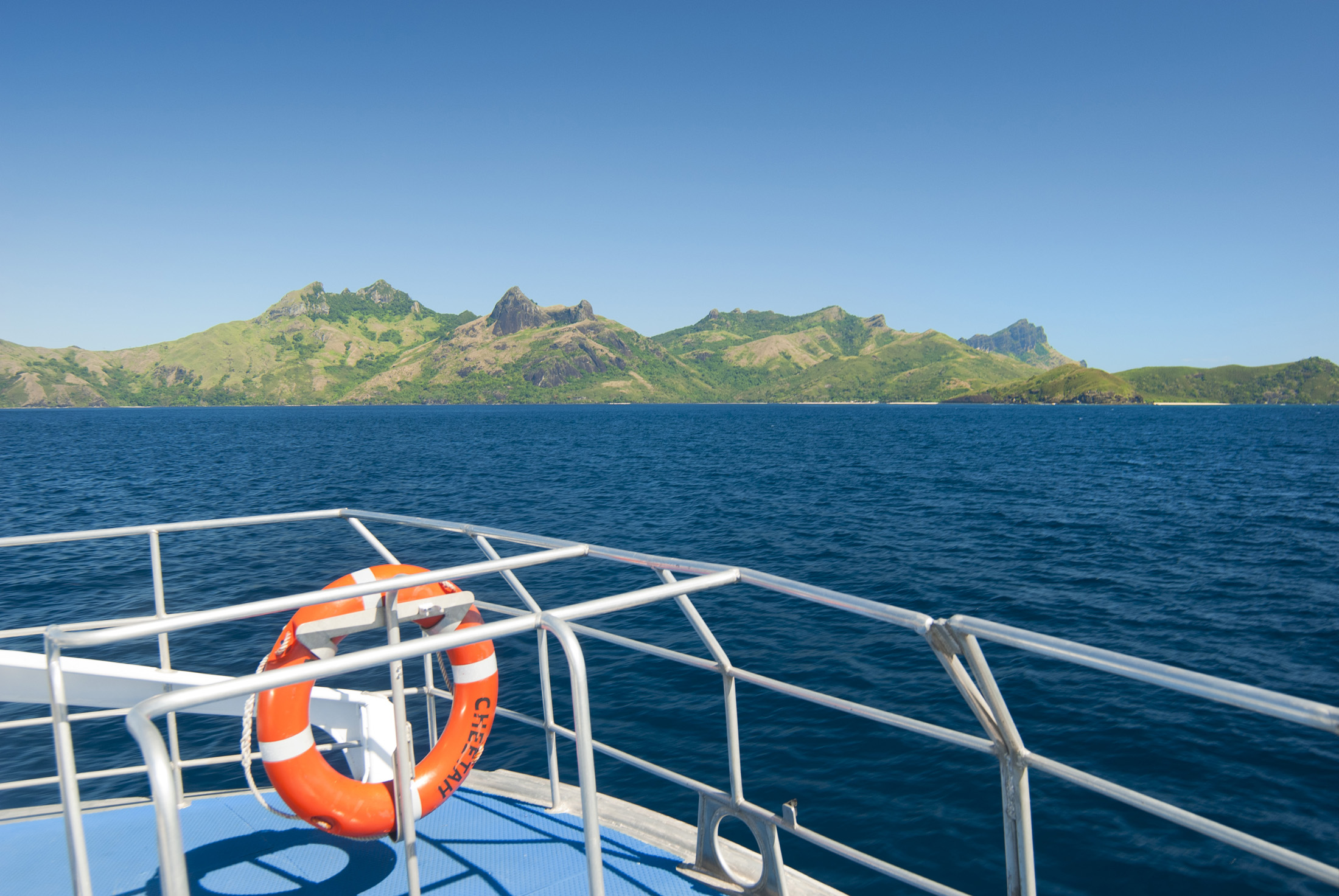 an image of Life ring on the railing of a boat cruising out at sea with Way island in Fiji in the background