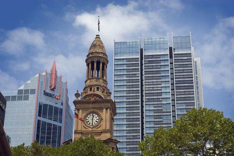 The top cupola of the historic Sydney town hall building and clock with surrounding trees and city.