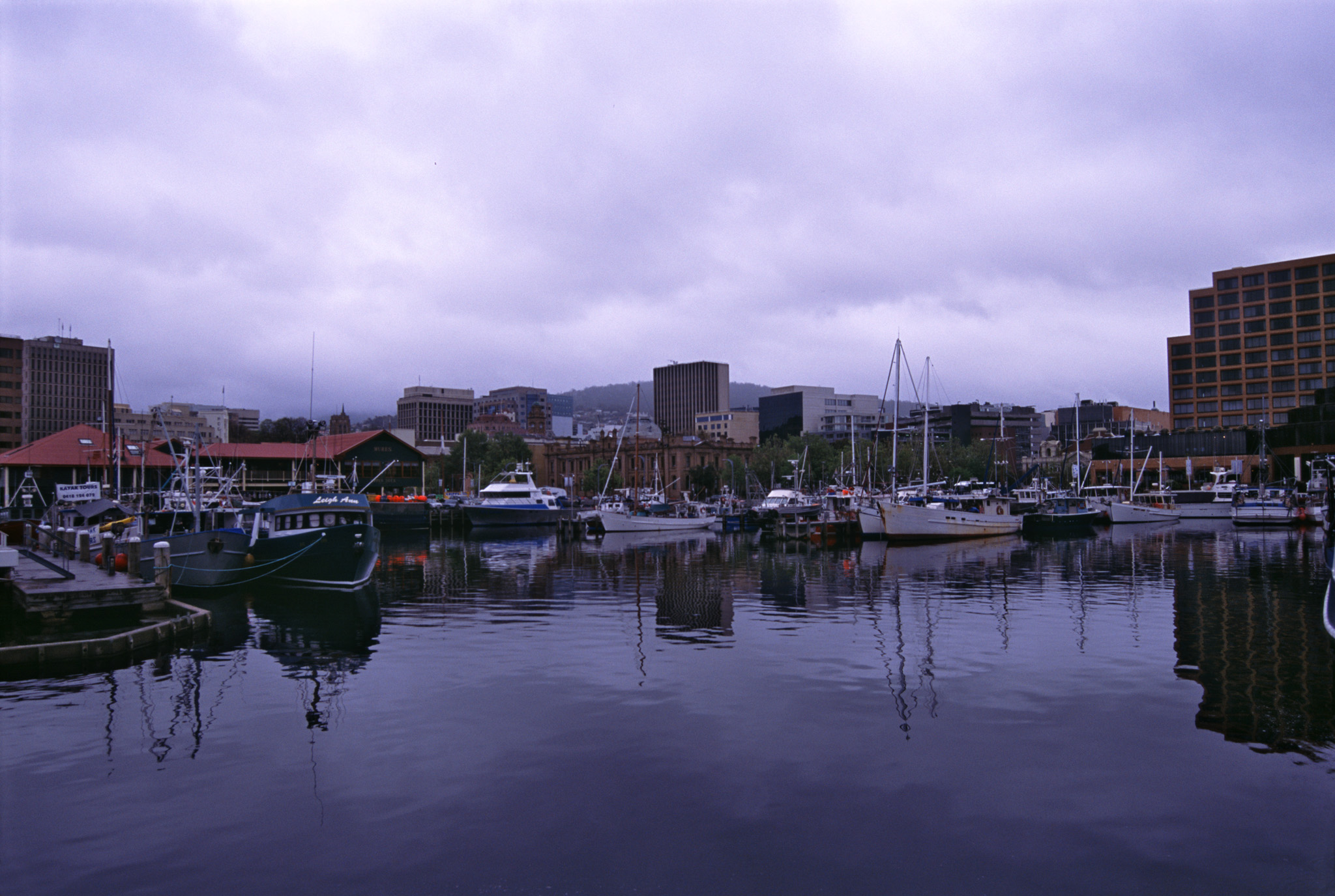 an image of Hobart harbor, Tasmania on the Derwent River with a variety of ships and boats moored at the quays in sheltered water on a cloudy day