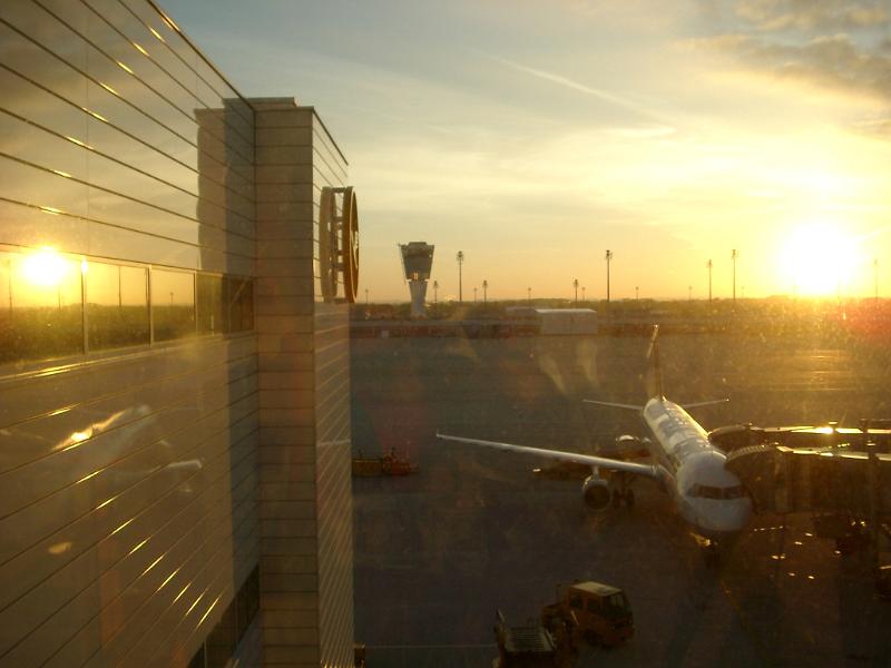Airport at sunset with a view along the exterior of the building onto the apron and an aircraft loading for departure