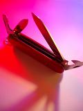 Swiss army knife opened to display the tools and gadgets in colorful red, pink and purple light with copyspace