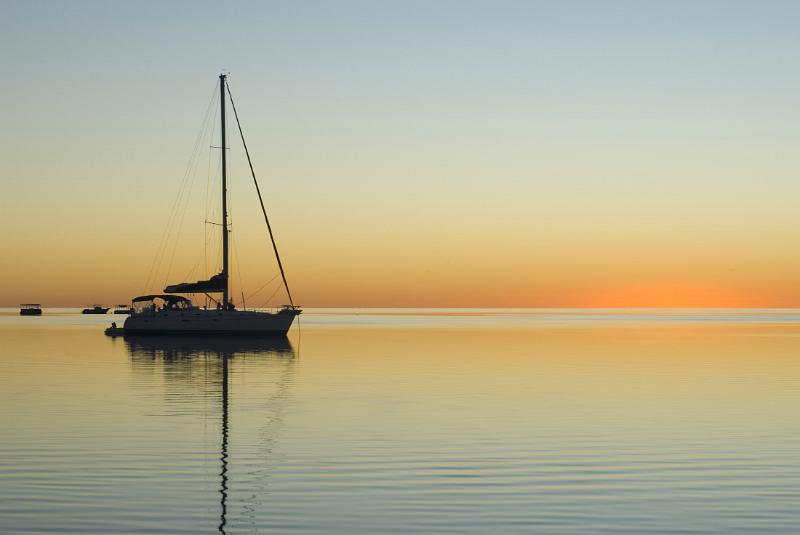 sunset over calm tropical waters with the silhouette of a sailing yacht