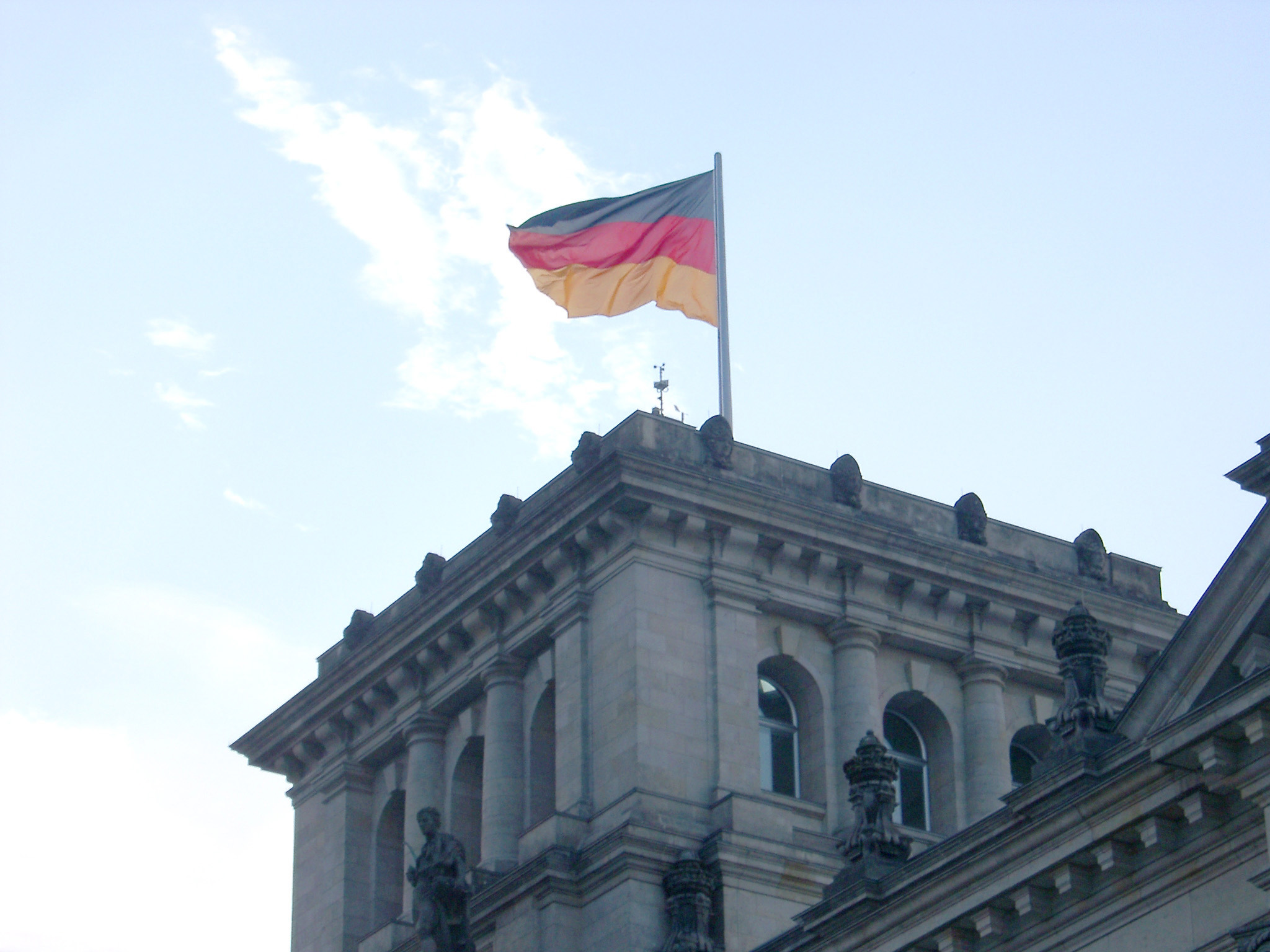 an image of German flag flying over the Reichstag building in Berlin, the seat of the German government, against a sunny blue sky
