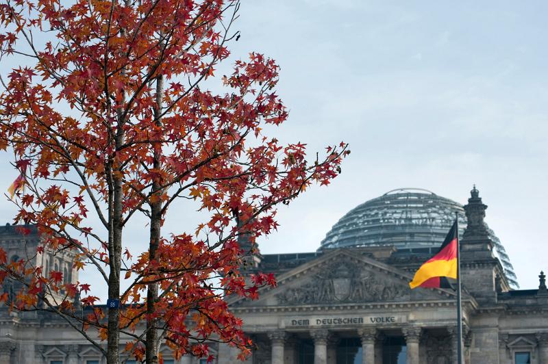 the reichstag parliament building in berlin with a german flag in the distance