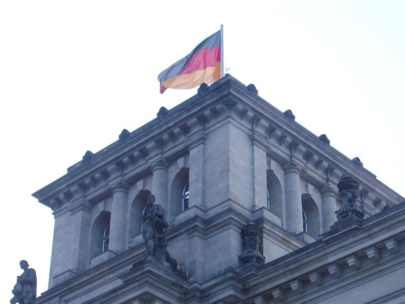 German flag flying at the Reichstag Building, the seat of the government in Berlin, against a bright sky