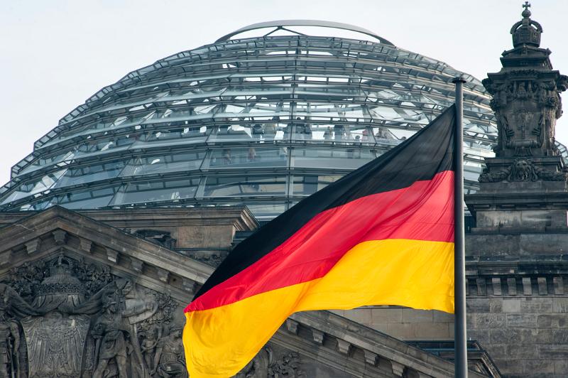 red black and gold colors of the German national flag with the Reichstag german parliament building and dome to the rear