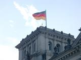 German flag flying over the Reichstag building in Berlin, the seat of the German government, against a sunny blue sky