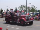Historic vintage Canadian fire truck driving through the streets with firefighters waving at seated crowds watching the parade