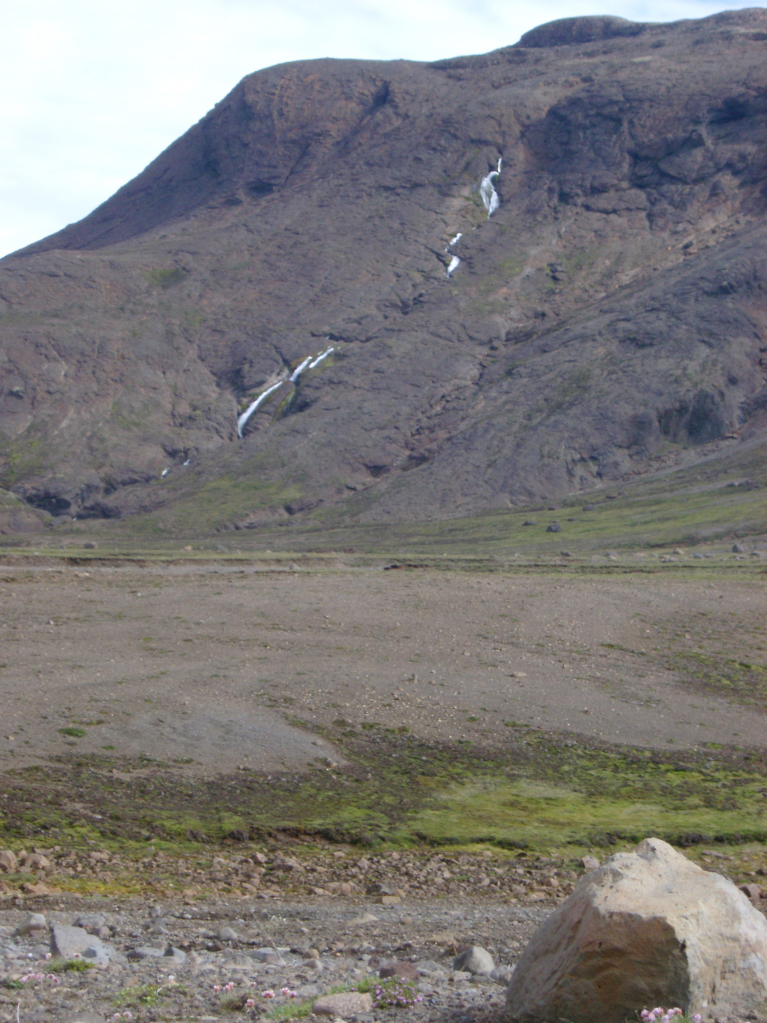 an image of Desolate volcanic mountain landscape in Iceland with a river flowing down a mountain peak onto the plains below