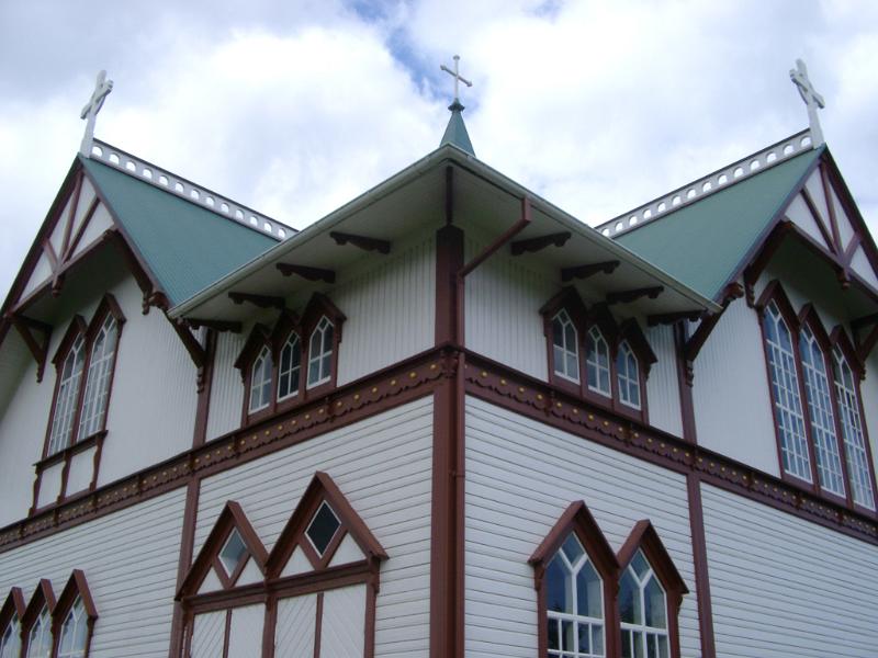 Exterior of the church in Husavik in Iceland with ornate windows and a roof adorned with crosses against a cloudy blue sky
