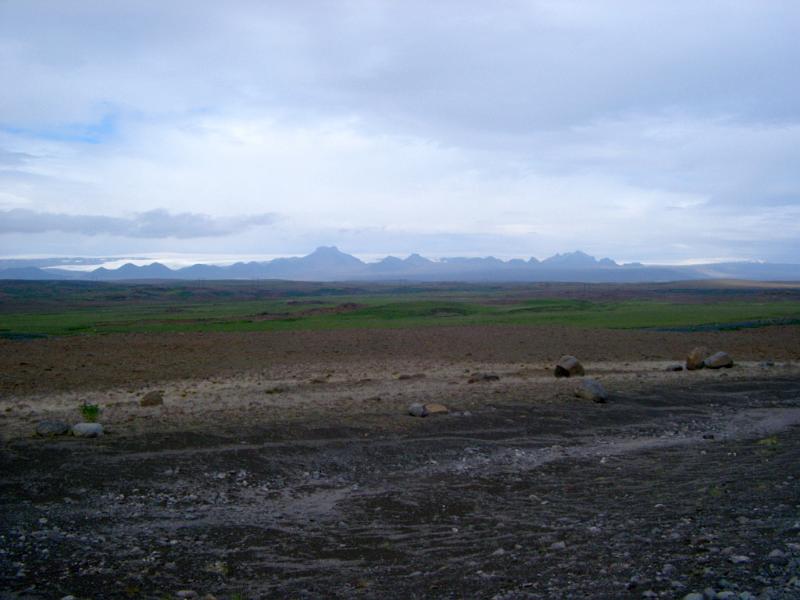 Remote Icelandic landscape with a stony path leading past a river with a range of volcanic mountain peaks in the distance
