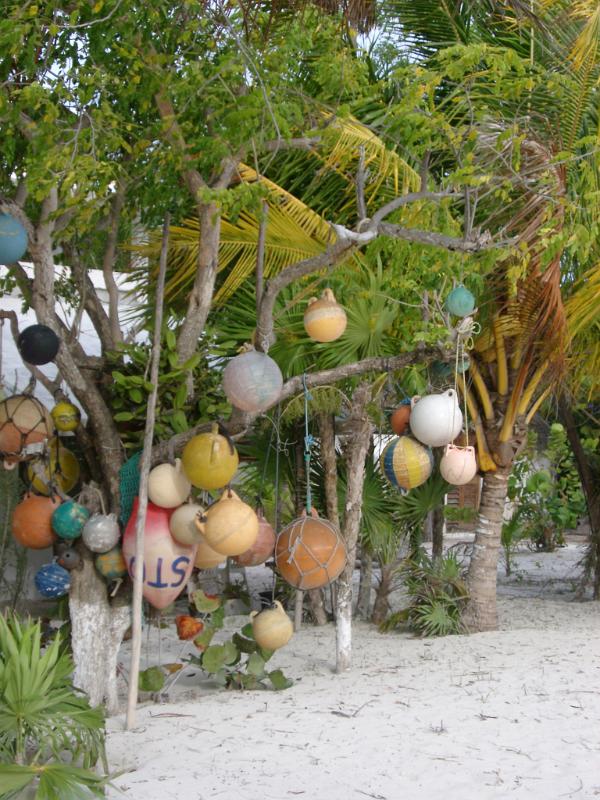 Colorful plastic fishing floats hanging from a wooden frame below palm trees on the golden sand of a tropical beach