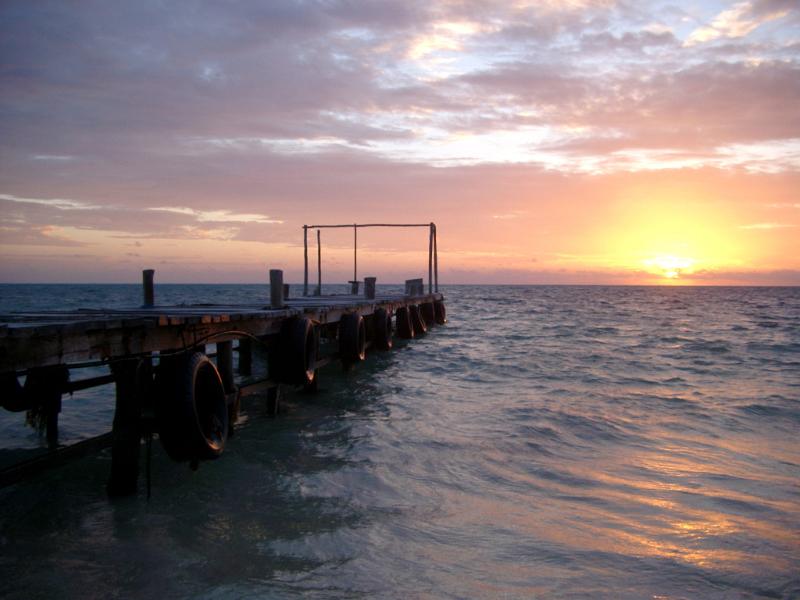 Wooden jetty at sunrise, Mexico Wooden jetty lined with a row of old tyres for mooring at sunrise with the glowing orb of the sun appearing above the ocean, Mexico