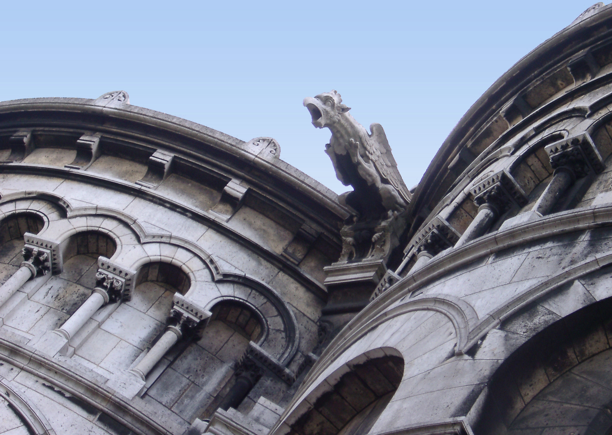 an image of Old Vintage Gargoyle Sculpture on the roof of sacre coeur, Isolated on Light Blue Sky Background.