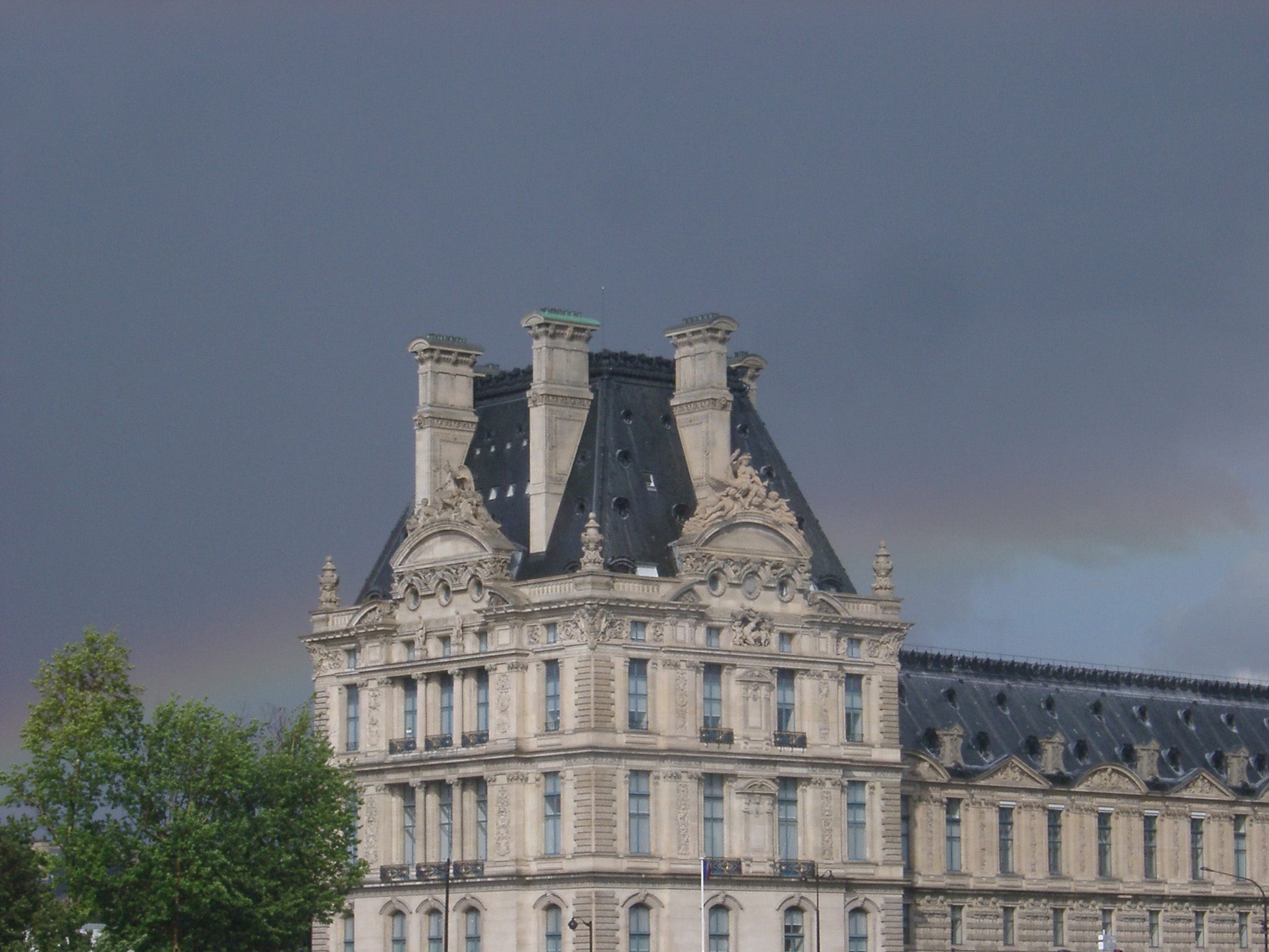 an image of Paris rainbow in a rainy stormy grey sky behind an imposing historical urban stone building
