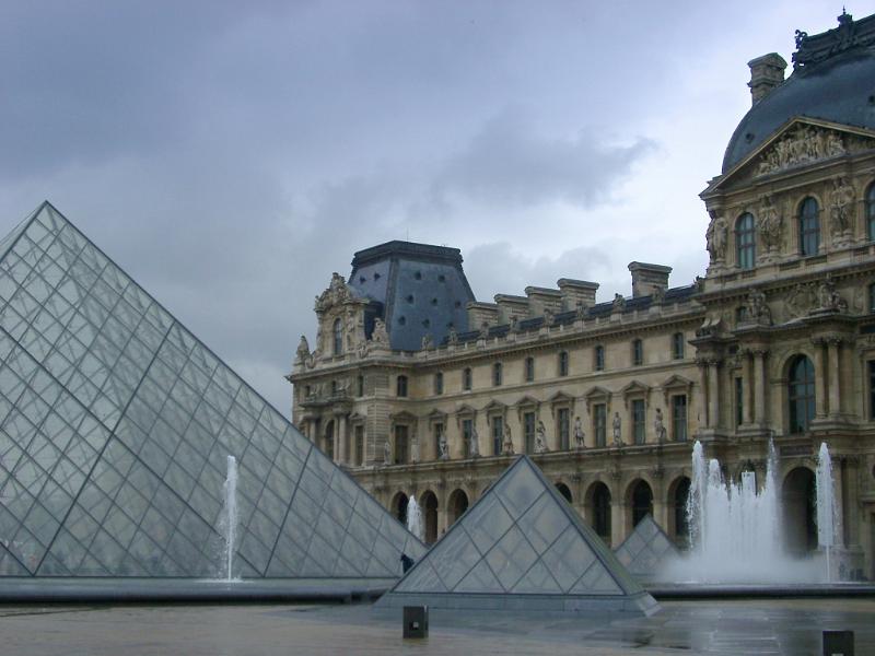 Courtyard of the Louvre in Paris showing the ornamental fountains and glass modern pyramids backed by the stone facade of the museum