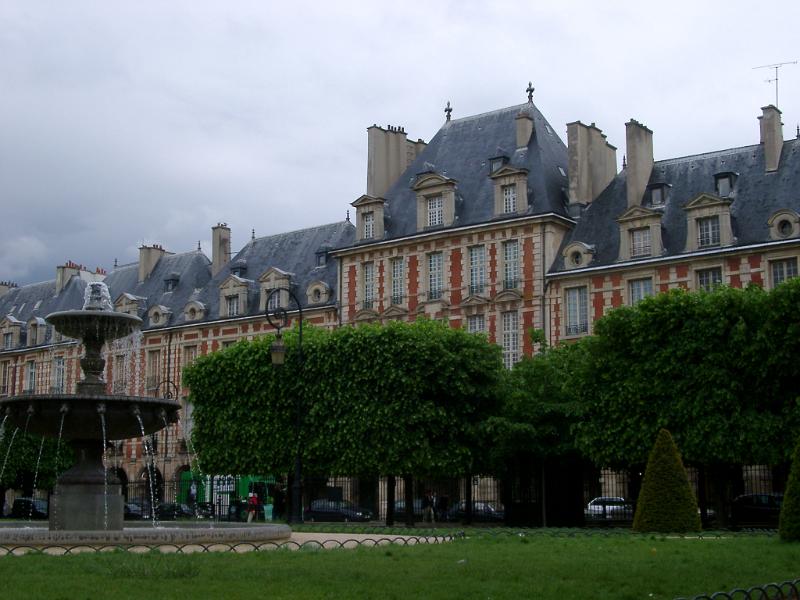 Green Landscape with Trees and Water Fountain Fronting Famous Vintage Place de Vosges Buildings. Isolated on Lighter Blue Gray Sky Background.