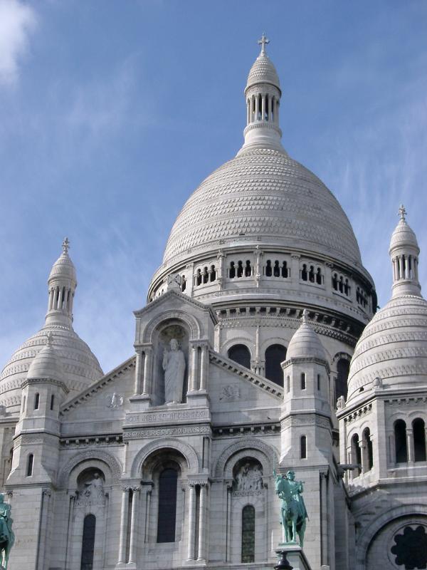 View of the white facade and domes of the iconic Sacre Couer Cathedral, butte Montmarte, Paris against a blue sky in a travel concept