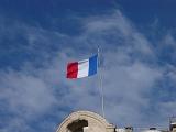 The Tricolor or French National Flag flying from a rooftop against a cloudy hazy blue sky with copyspace