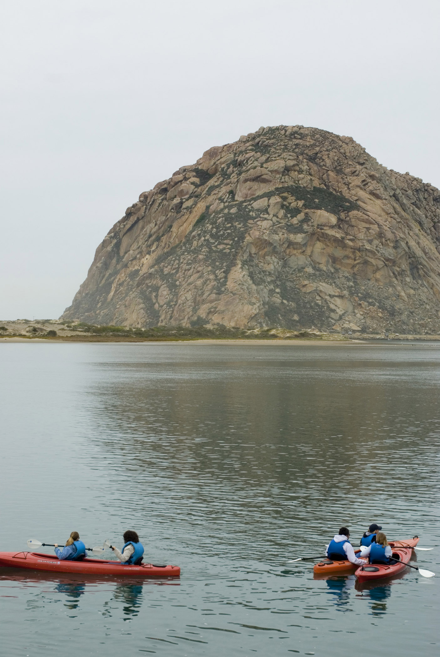 an image of Tourists Kayaking at Morro Bay with Big Morro Rock on Lighter Blue Sky Background.