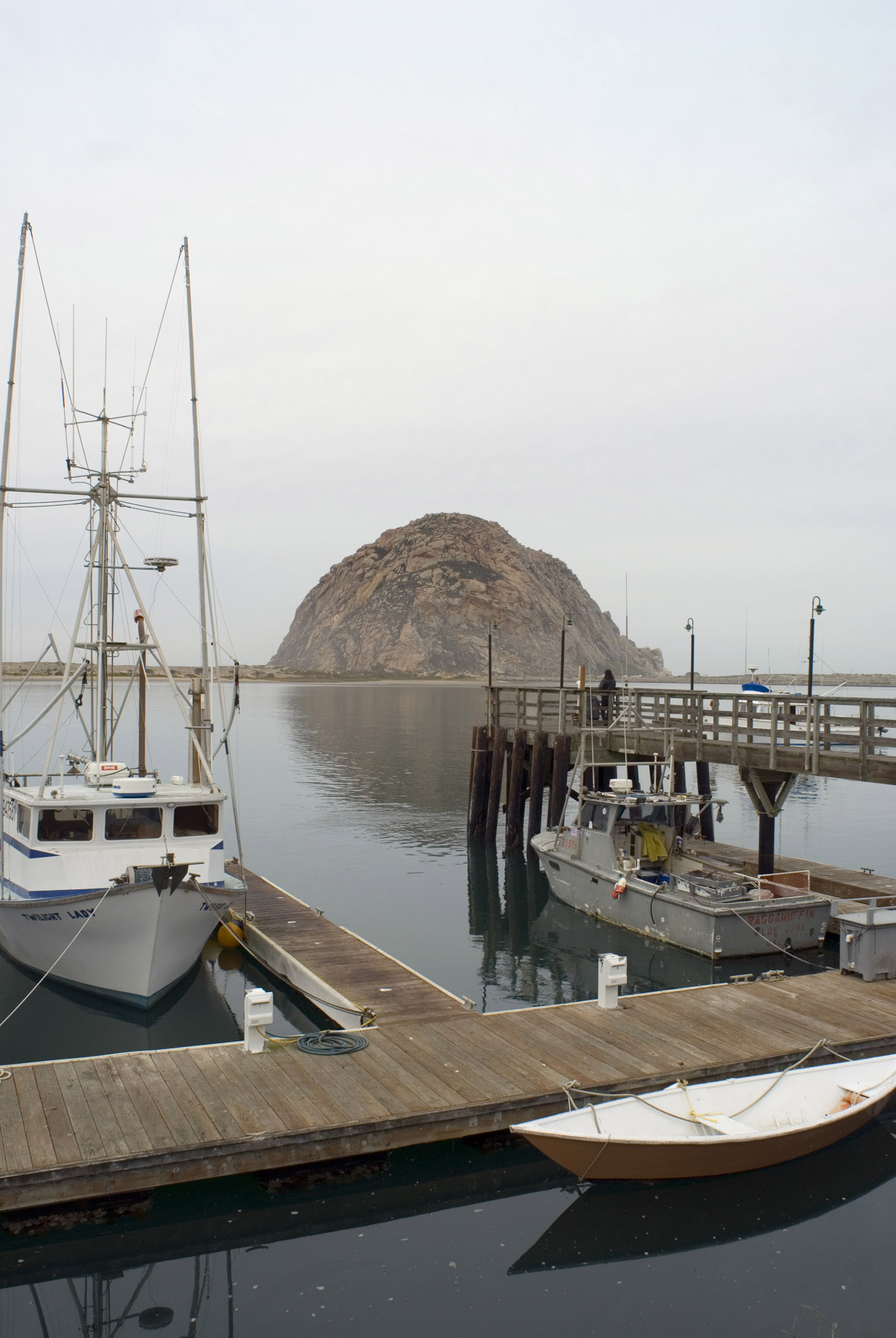 an image of Small Boats at the Dock of Beautiful Morro Bay, Captured with Famous Big Rock. Isolated on Light Gray Sky Background.