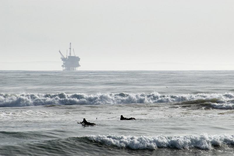 Offshore oil rig in the Gulf of Mexico on a misty horizon across a calm ocean with two surfers in the foreground