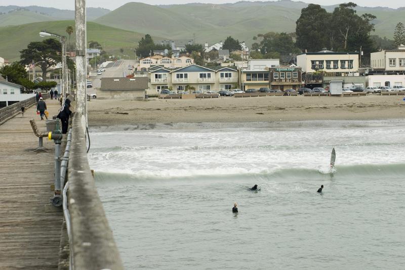 View along the wooden jetty or pier in Cayucos State Beach Park looking towards the beach with surfers in the water below
