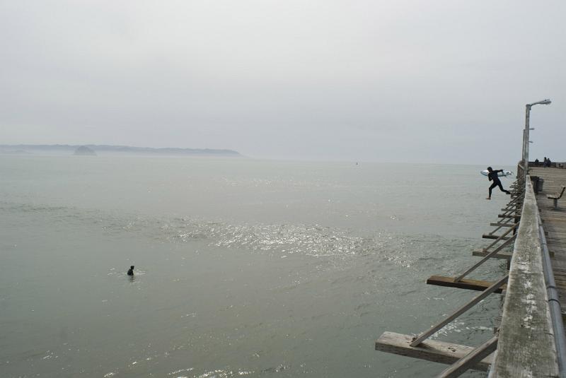 Beach Surfers at Famous Cayucos Pier in California. Captured in Extensive View on Foggy Sky Background.
