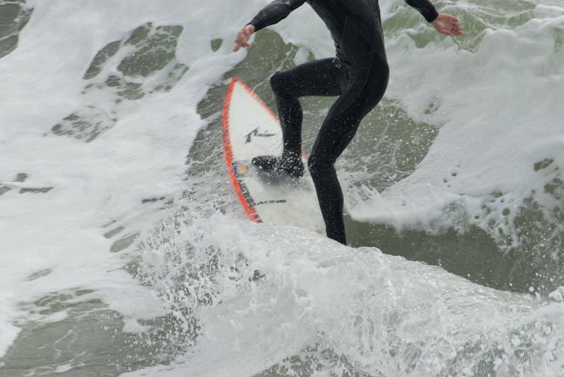 California surfer showing the legs of a person in a wetsuit balancing on a surfboard in a breaking wave with white surf