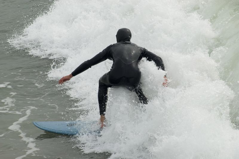 California surfer with a back view of a surfer in a wetsuit riding a breaking wave on a surfboard