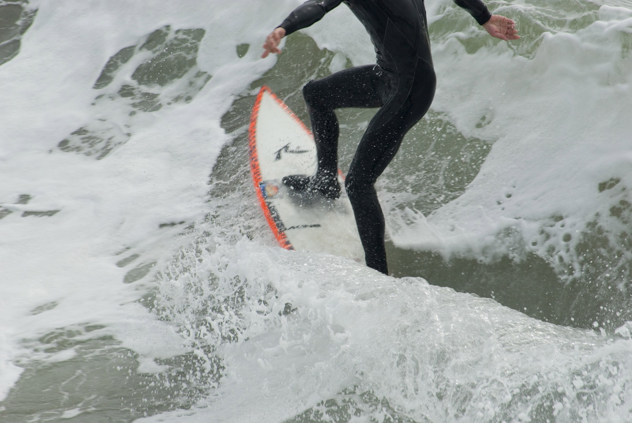 an image of California surfer showing the legs of a person in a wetsuit balancing on a surfboard in a breaking wave with white surf