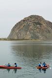 Tourists Kayaking at Morro Bay with Big Morro Rock on Lighter Blue Sky Background.