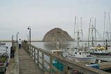 Vintage Wooden Bridge, Boats on the Dock and Famous Big Rock at Morro Bay. Isolated Lighter Blue Gray Sky Background.