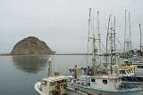 Boats at Morro Bay Dock and Famous Morro Rock Afar. Against an overcast grey sky background.